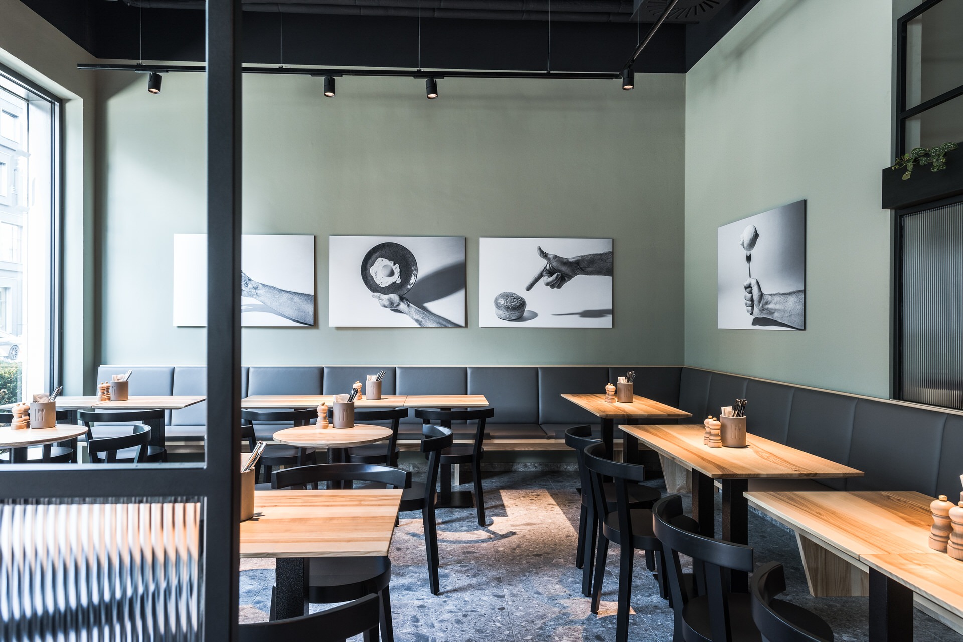 Innenansicht von "Ruff's Burger" mit Holztischen, schwarzen Stühlen, grauer Polsterbank, grüner Wand mit Schwarz-Weiß-Fotografien.