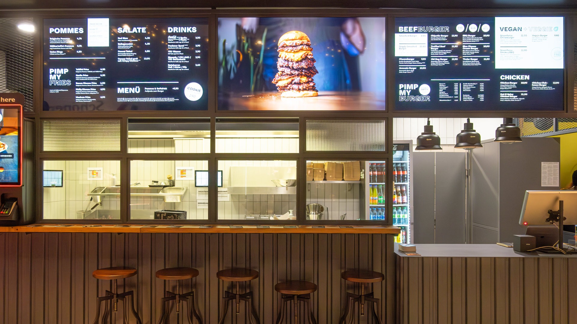 Thekenbereich von "Ruff's Burger" mit Barhockern, beleuchteter Menütafel, Burger-Foto und Blick in die offene Küche.