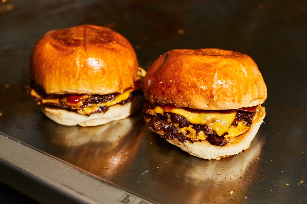 Zwei saftige Smash Burger mit geschmolzenem Käse auf einer Grillplatte.