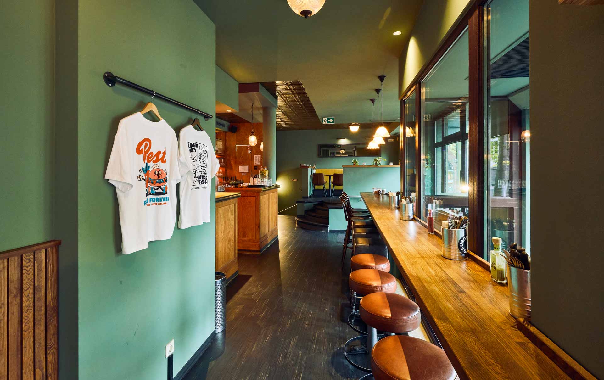 Barbereich von "Otto's Burger" mit Holztheke, offenen Regalen, Hängelampen, Fliesenwand und dekorativer Decke.