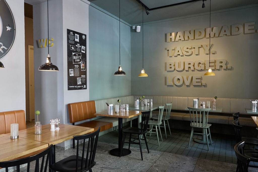 Innenansicht auf einen Sitzbereich mit Tischen, Stühlen und einem Spruch an der Wand.